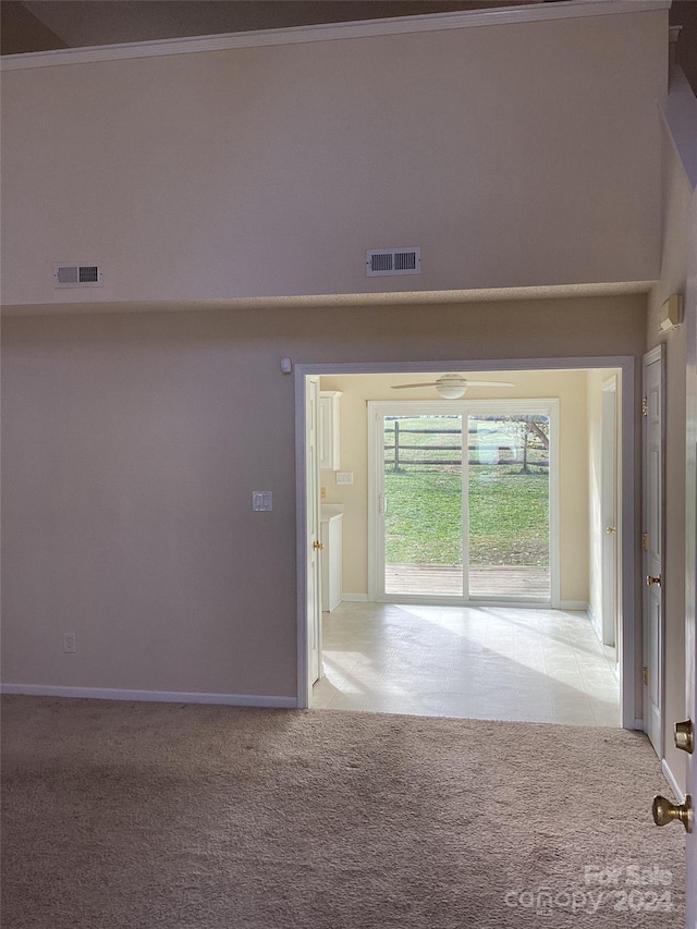 empty room with light carpet, crown molding, and a high ceiling