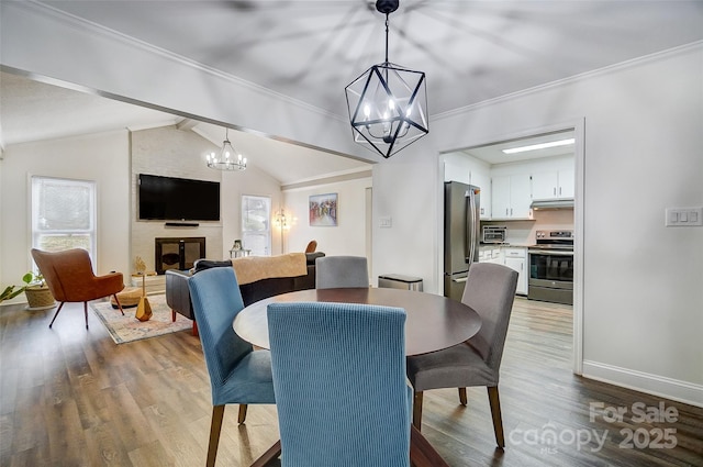 dining space featuring a fireplace, lofted ceiling with beams, crown molding, an inviting chandelier, and light hardwood / wood-style flooring