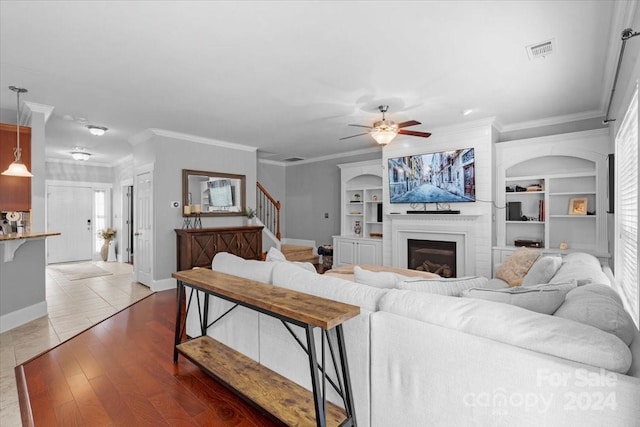 living room featuring hardwood / wood-style floors, built in features, ceiling fan, and crown molding