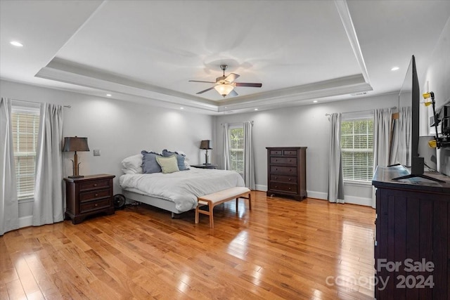 bedroom with light hardwood / wood-style floors, a raised ceiling, and multiple windows