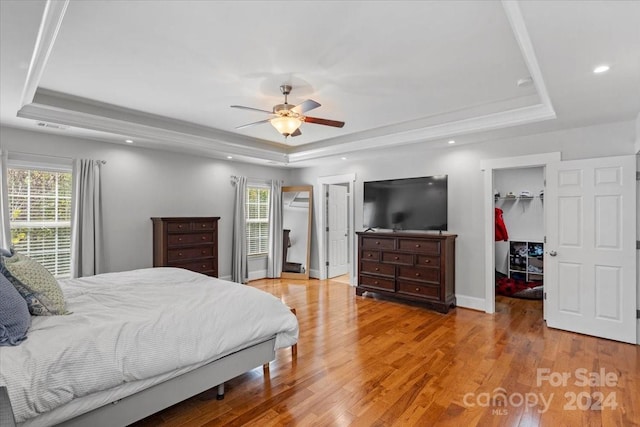 bedroom featuring a tray ceiling, a spacious closet, hardwood / wood-style floors, and ceiling fan