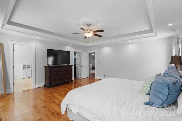 bedroom featuring ceiling fan, a tray ceiling, a walk in closet, a closet, and hardwood / wood-style flooring