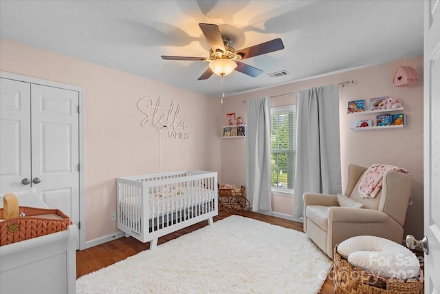 bedroom with ceiling fan, a closet, a crib, and hardwood / wood-style flooring