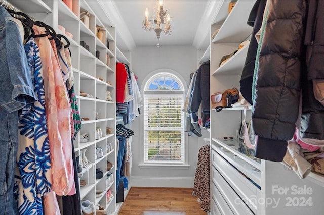 walk in closet with light hardwood / wood-style floors and an inviting chandelier