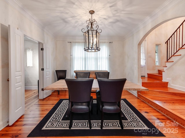 dining area featuring arched walkways, wood finished floors, stairs, ornamental molding, and an inviting chandelier