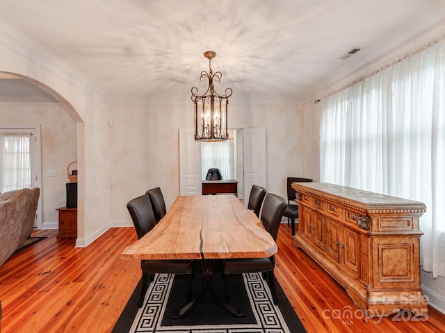 dining room with light wood finished floors, plenty of natural light, arched walkways, and ornamental molding