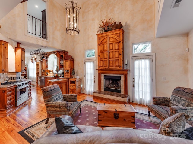 living room featuring light wood-style floors, a wealth of natural light, visible vents, and a fireplace with raised hearth