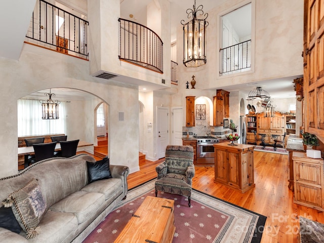 living area with light wood-type flooring, visible vents, a chandelier, and arched walkways