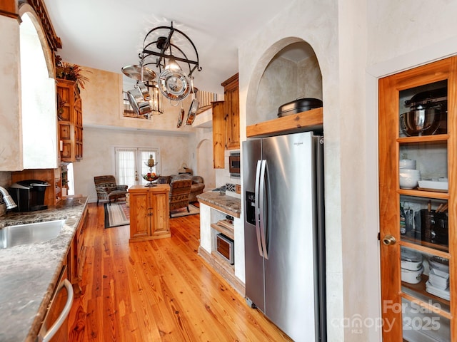 kitchen featuring brown cabinets, stainless steel appliances, a sink, a chandelier, and light wood-type flooring