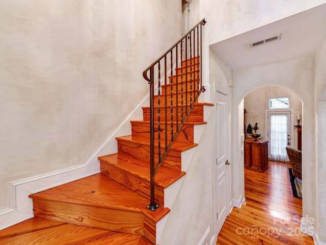 stairway featuring arched walkways, visible vents, and wood finished floors