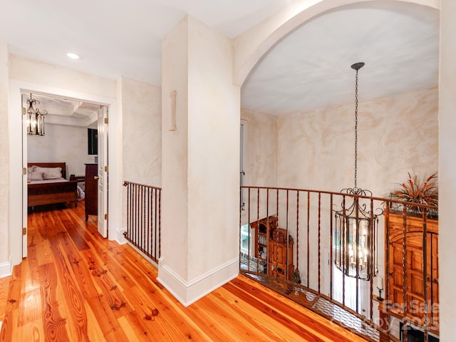 hallway featuring an inviting chandelier, baseboards, arched walkways, and wood finished floors