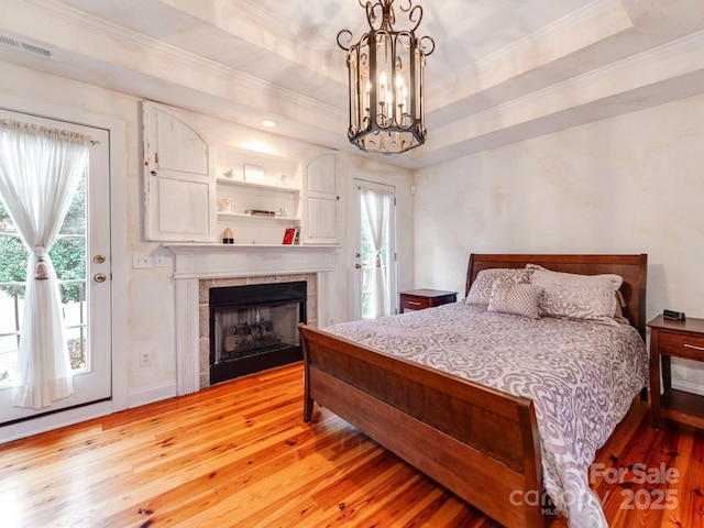 bedroom with access to exterior, a tray ceiling, visible vents, and light wood finished floors