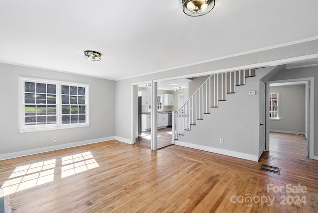 unfurnished living room with light wood-type flooring and ornamental molding