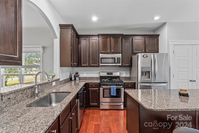 3157 Delaware Dr, Denver, NC 28037 - kitchen featuring arched walkways, light stone counters, appliances with stainless steel finishes, dark brown cabinets, and a sink