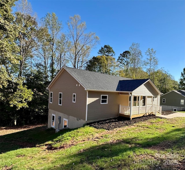 view of side of home featuring a porch, a lawn, and a shingled roof