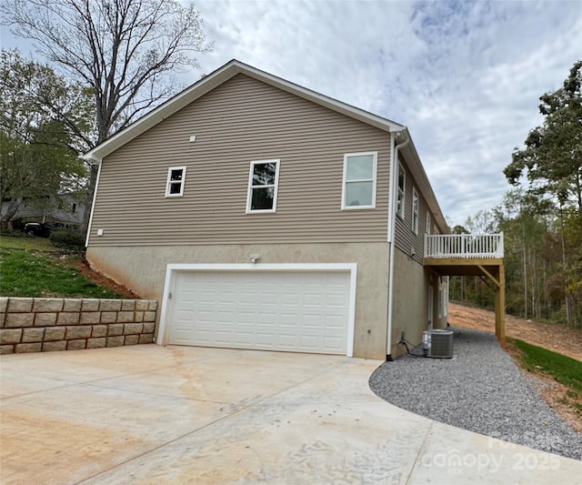 view of side of property with an attached garage, stucco siding, central AC, and concrete driveway