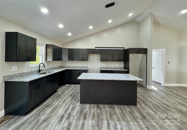 kitchen with light wood finished floors, a kitchen island, light stone counters, hanging light fixtures, and a sink