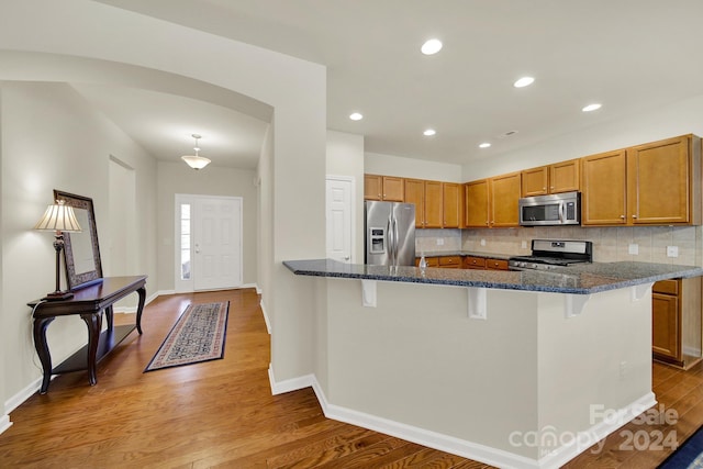 kitchen featuring light hardwood / wood-style flooring, stainless steel appliances, dark stone counters, and a breakfast bar