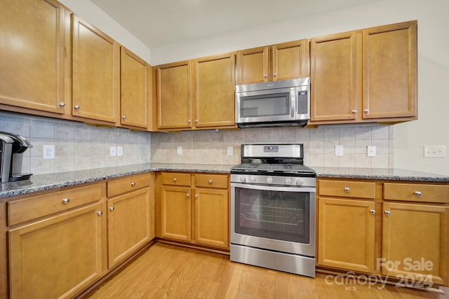 kitchen featuring decorative backsplash, appliances with stainless steel finishes, light stone counters, and light wood-type flooring