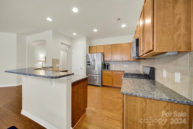 kitchen featuring a kitchen bar, light wood-type flooring, dark stone counters, and stainless steel appliances