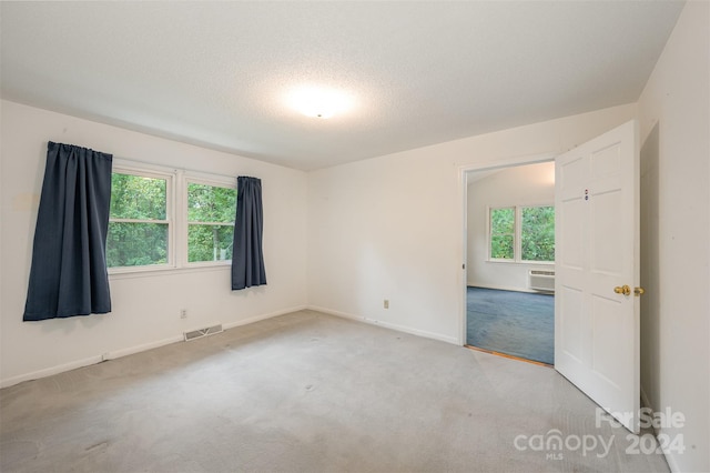 carpeted empty room featuring a wall mounted air conditioner, a textured ceiling, and plenty of natural light