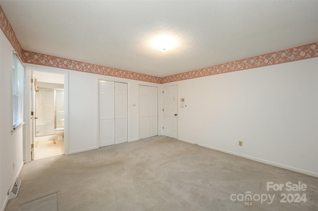 unfurnished bedroom featuring connected bathroom, light carpet, multiple closets, and a textured ceiling