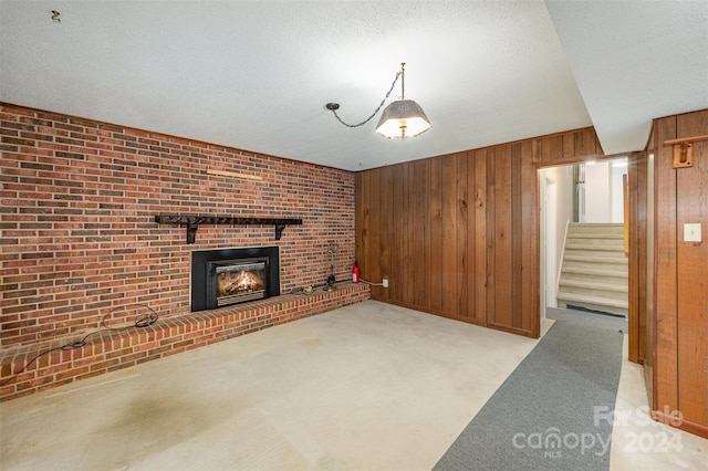 unfurnished living room featuring light colored carpet, a textured ceiling, wooden walls, and a brick fireplace