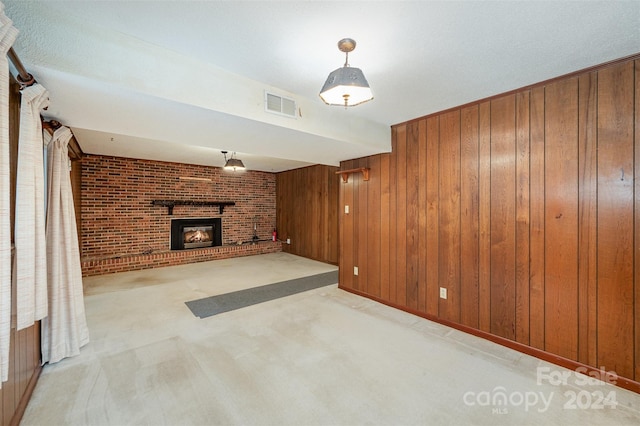 unfurnished living room with brick wall, a brick fireplace, wooden walls, and light colored carpet