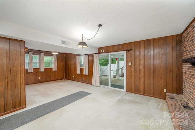 unfurnished living room with light carpet, wood walls, plenty of natural light, and brick wall