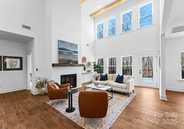 living room featuring beam ceiling, a fireplace, a towering ceiling, and wood-type flooring