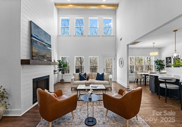 living room featuring a high ceiling, dark hardwood / wood-style floors, a fireplace, beam ceiling, and a chandelier