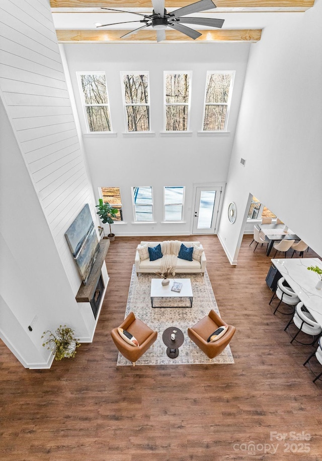 living room with beamed ceiling, dark hardwood / wood-style floors, ceiling fan, and a high ceiling