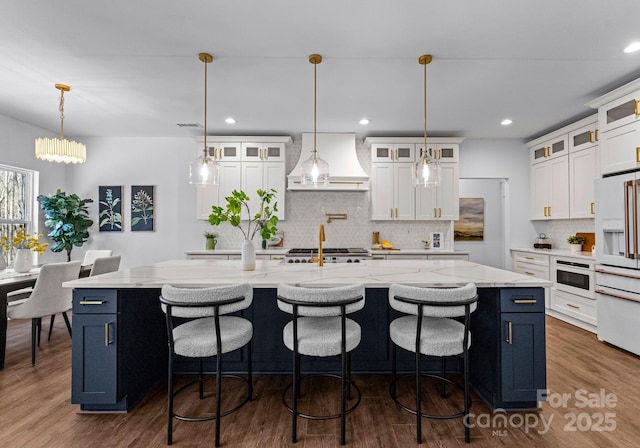 kitchen featuring hanging light fixtures, custom range hood, white fridge with ice dispenser, and a spacious island