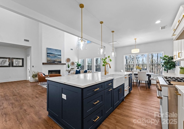 kitchen featuring a center island with sink, blue cabinets, sink, hanging light fixtures, and a fireplace