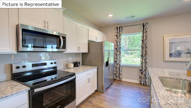 kitchen with light stone countertops, white cabinets, appliances with stainless steel finishes, and light wood-type flooring