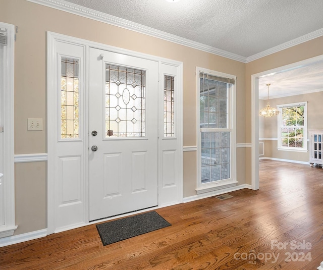 foyer with a notable chandelier, a textured ceiling, hardwood / wood-style flooring, and crown molding