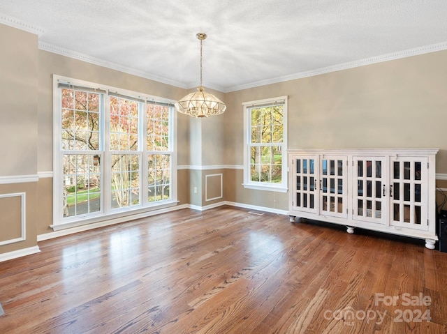 unfurnished dining area featuring hardwood / wood-style floors, a textured ceiling, crown molding, and an inviting chandelier