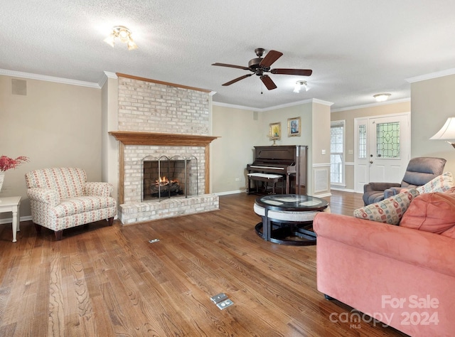 living room featuring a brick fireplace, hardwood / wood-style flooring, a textured ceiling, and crown molding