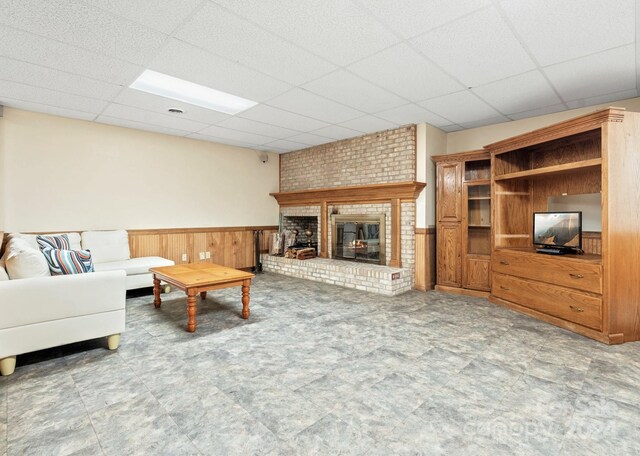 living room with a fireplace, wooden walls, and a drop ceiling