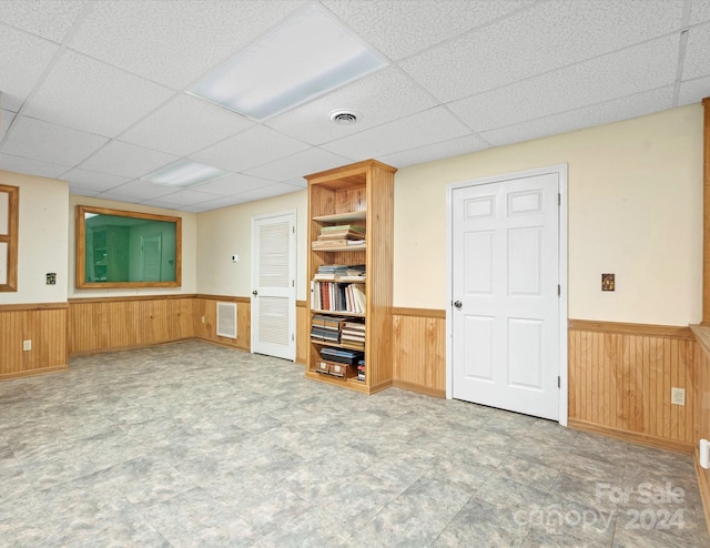 unfurnished living room with a paneled ceiling and wooden walls