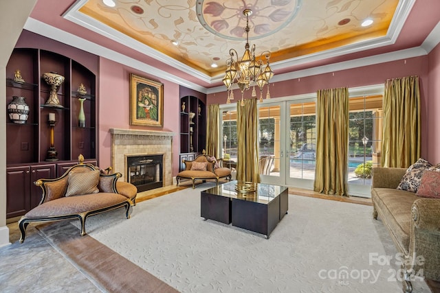 living room with an inviting chandelier, a tray ceiling, a brick fireplace, ornamental molding, and french doors