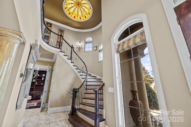 tiled foyer featuring baseboards, a high ceiling, ornamental molding, and stairs