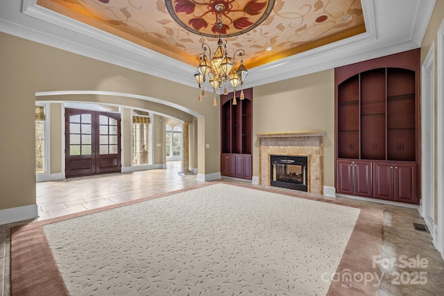 unfurnished living room with arched walkways, built in shelves, a tile fireplace, a tray ceiling, and an inviting chandelier