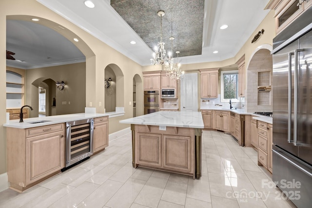 kitchen featuring a center island, a tray ceiling, stainless steel appliances, ornamental molding, and beverage cooler