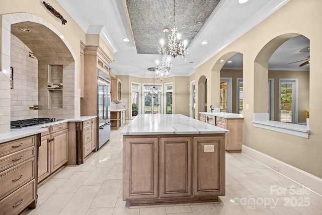 kitchen with a kitchen island, gas stovetop, ornamental molding, stainless steel built in fridge, and a raised ceiling