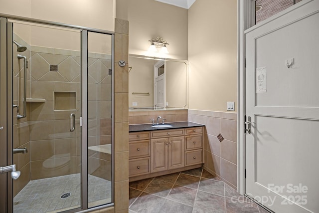 bathroom featuring vanity, tile walls, wainscoting, tile patterned floors, and a stall shower