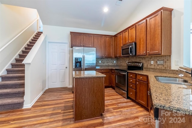 kitchen with light wood-type flooring, a kitchen island, sink, stainless steel appliances, and light stone countertops