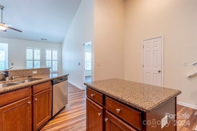 kitchen with sink, stainless steel dishwasher, a center island, light stone countertops, and light hardwood / wood-style floors