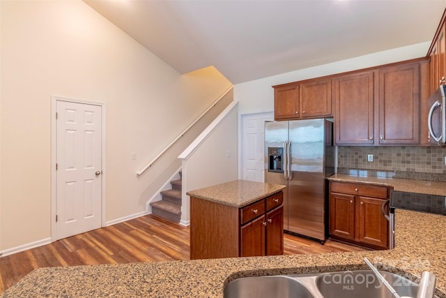 kitchen with light stone countertops, a center island, light hardwood / wood-style floors, appliances with stainless steel finishes, and backsplash