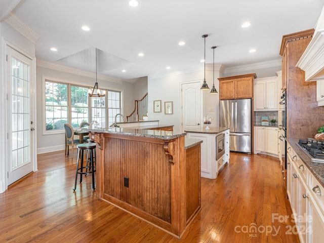 kitchen with a center island with sink, appliances with stainless steel finishes, a breakfast bar, light hardwood / wood-style floors, and decorative light fixtures